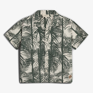 A short-sleeved shirt displays a green palm leaf pattern on a beige background. The shirt has buttons and a collar, suitable for casual settings. There's a small logo patch at the bottom.