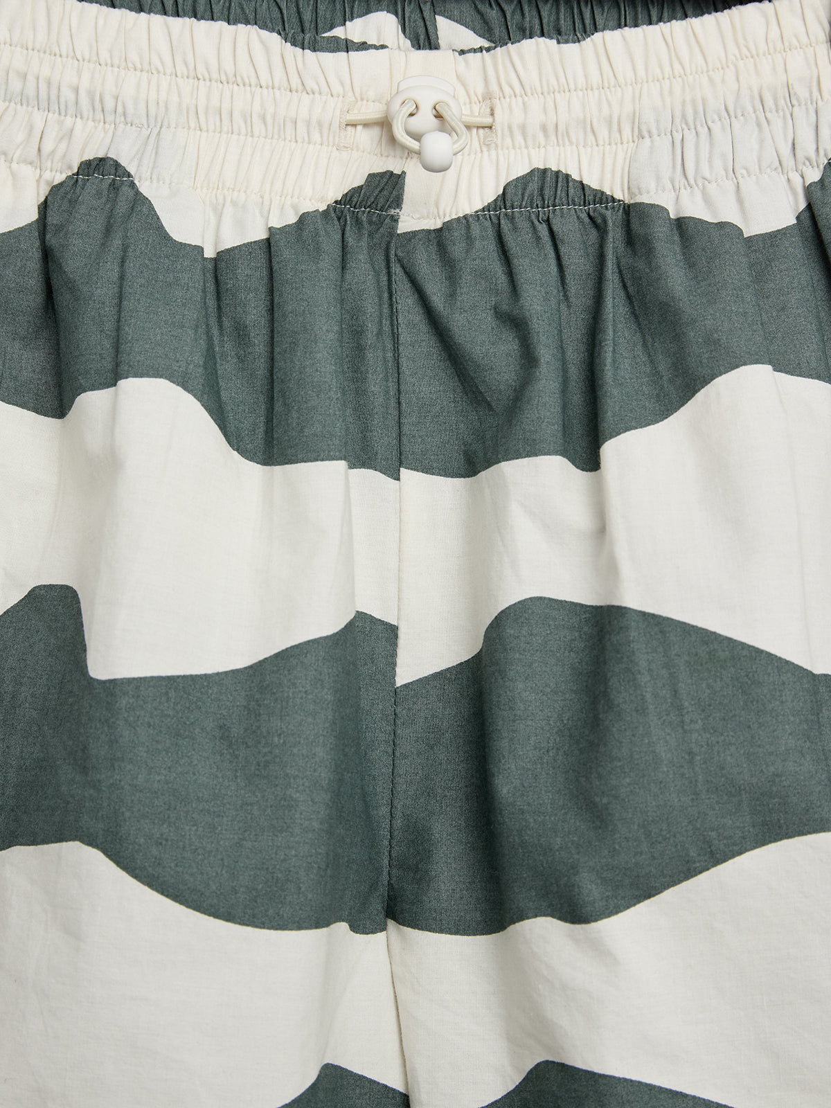 Elastic waistband shorts with a green and white wavy stripe pattern; a drawstring with a white plastic toggle is threaded through the waistband for adjustment.