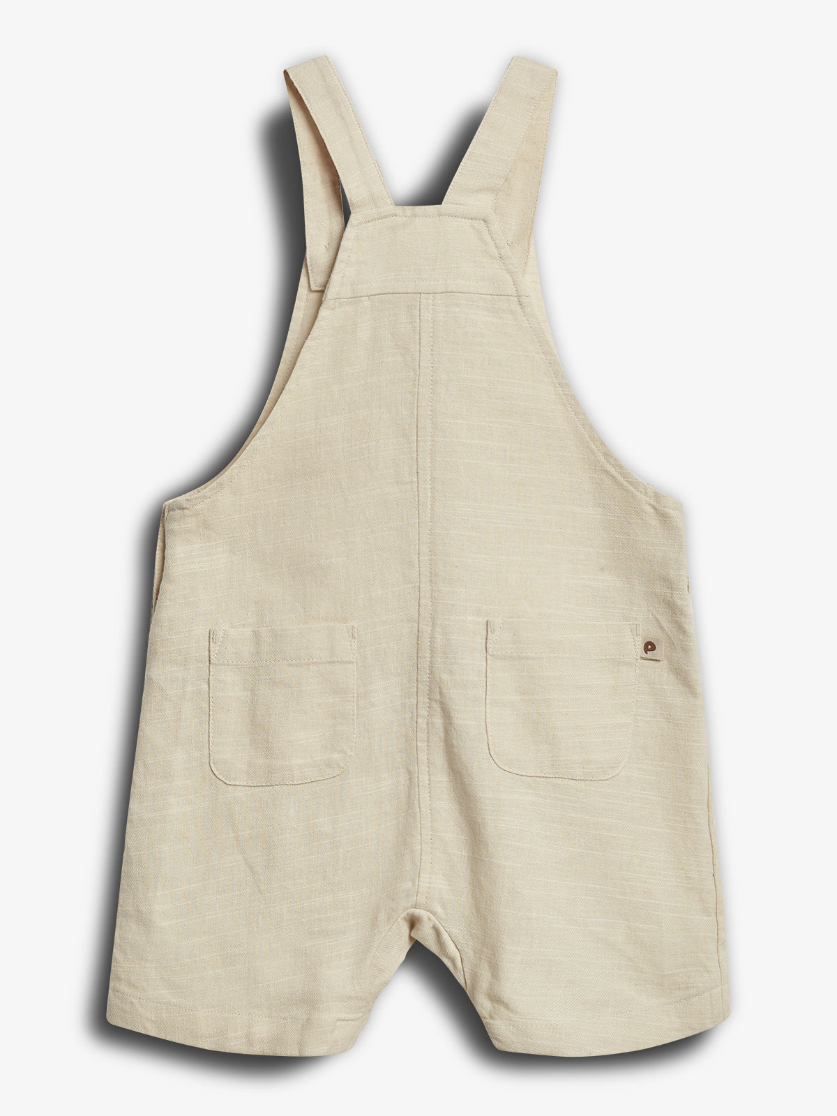 A beige linen romper with shoulder straps features two front pockets. The garment lies flat against a neutral background, emphasizing its casual, minimalist style.