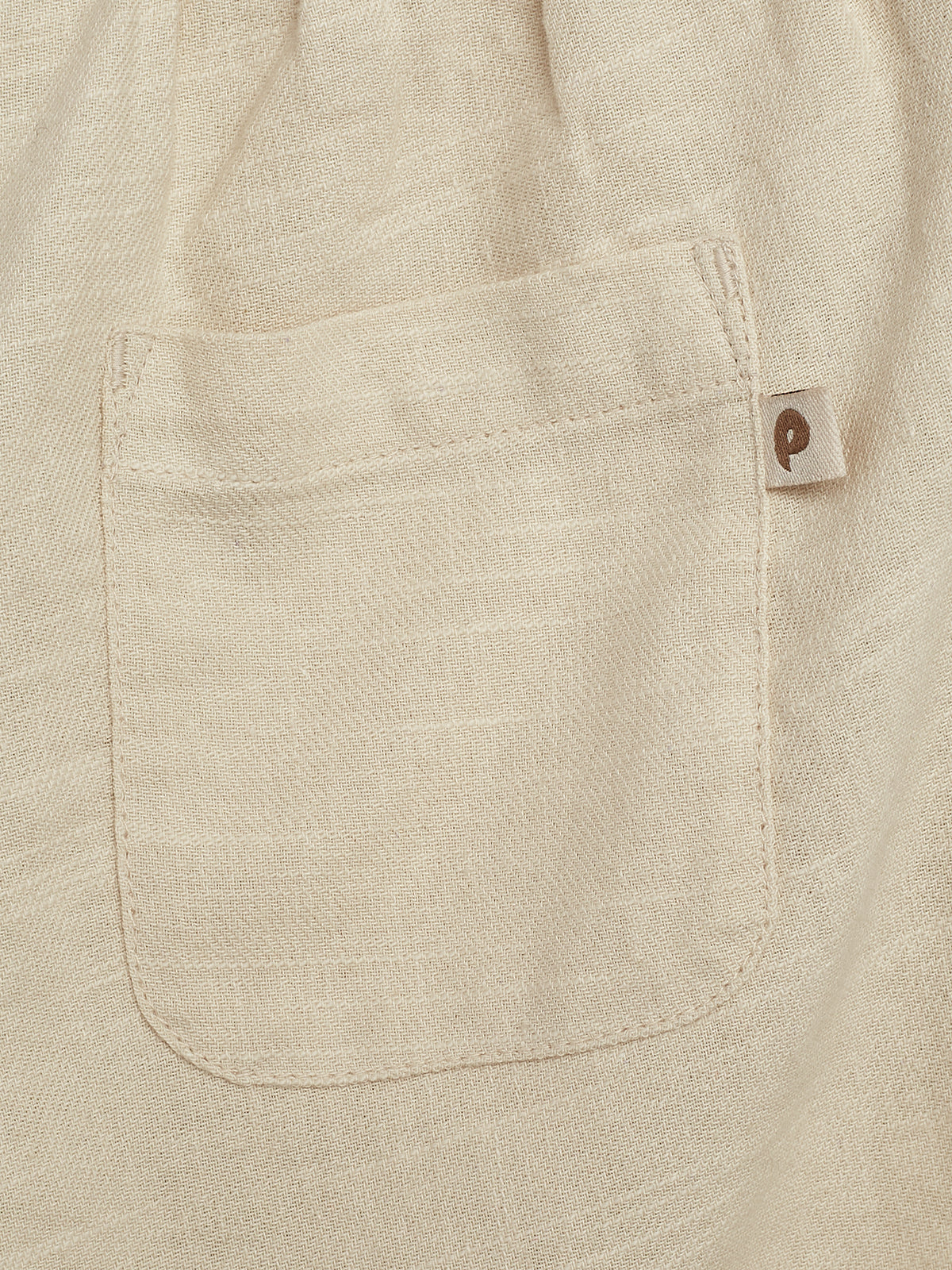 A beige fabric pocket is sewn onto a similar material background. It features a small attached tag with a lowercase letter "p" printed on it.