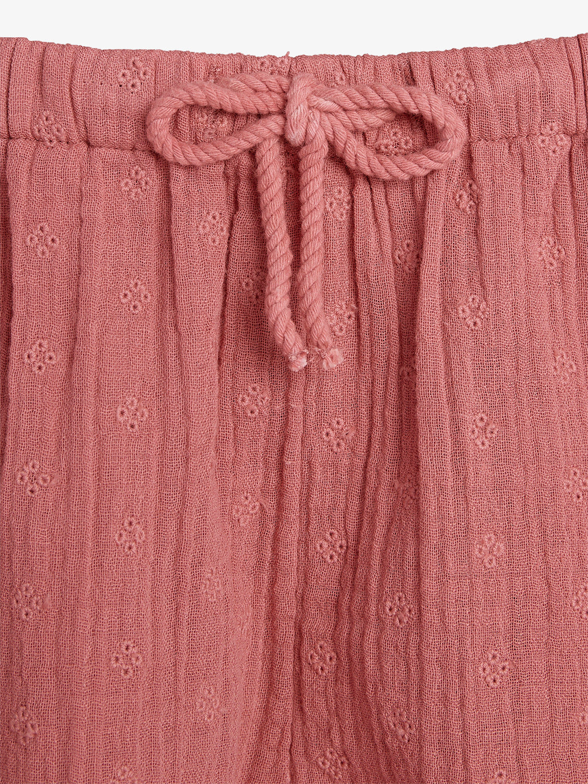 Pink textured fabric shorts feature a drawstring tie at the waistband. The material is adorned with small, subtle floral patterns, creating a delicate and comfortable appearance.