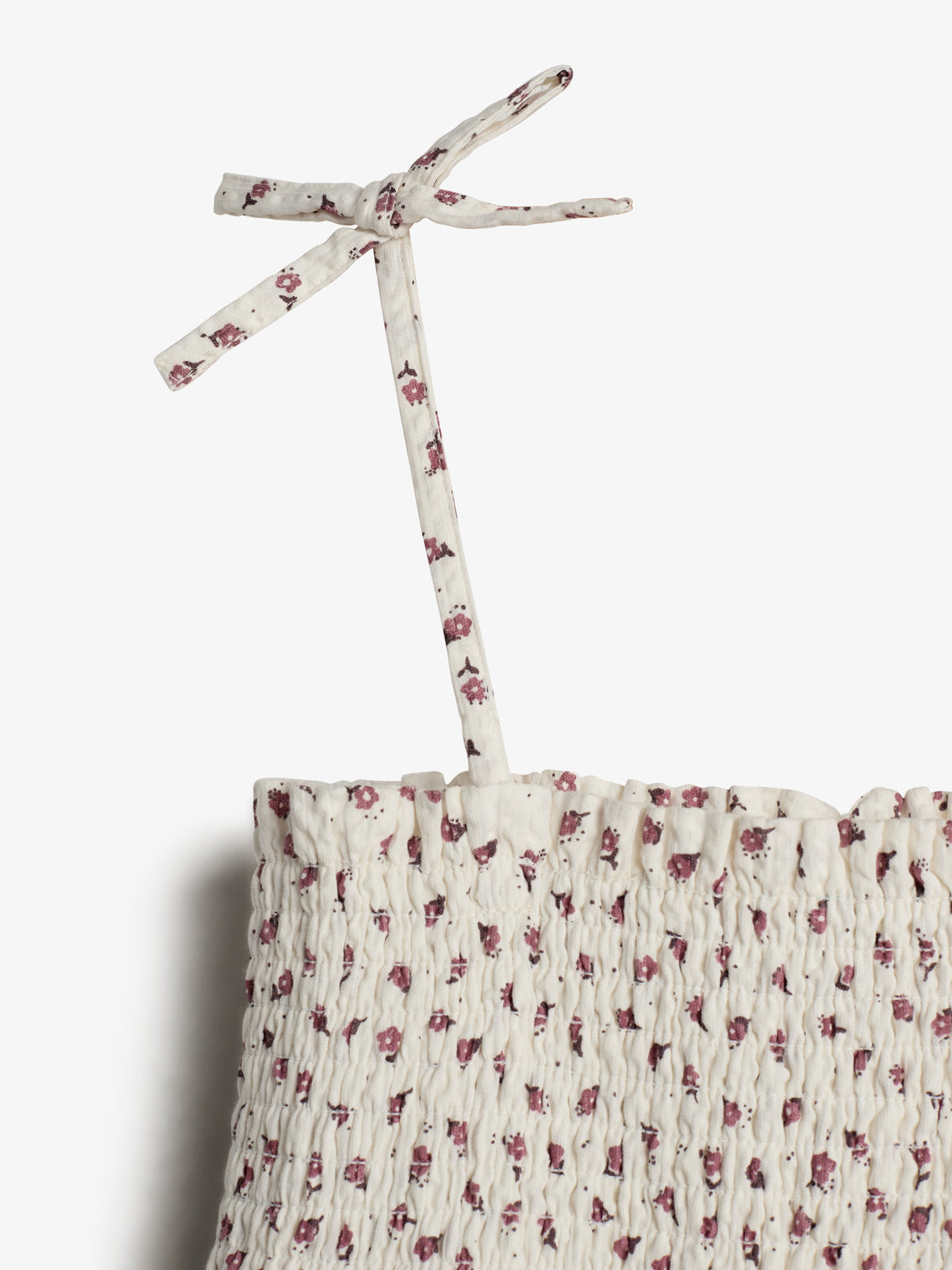 A fabric strap tied in a bow emerges from a smocked, off-white material featuring small maroon floral patterns, set against a plain white background.