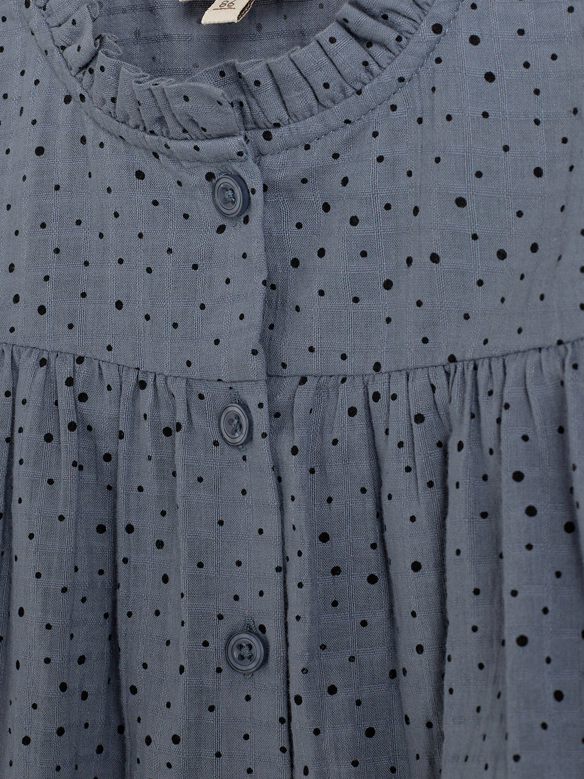 A blue, polka-dotted fabric features a button-down design with three visible buttons. The material has a textured appearance, gathered at seams, set against a softly pleated context.