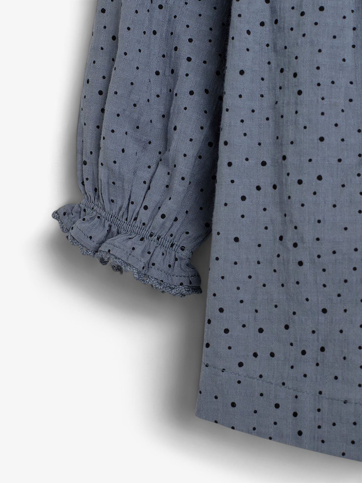 A gray fabric with black polka dots features a gathered, elasticated sleeve with ruffled cuffs, hanging against a plain background.