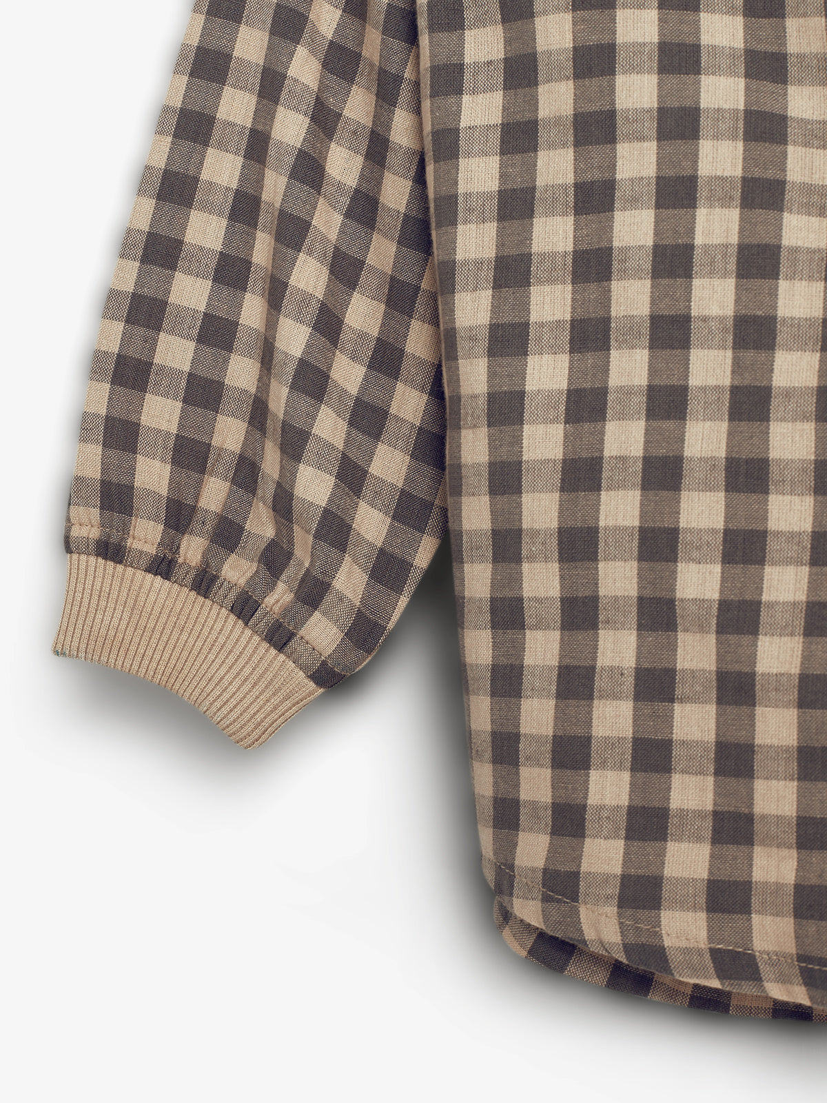 A checkered long-sleeve shirt with gray and beige squares rests against a plain white background. The shirt features ribbed cuffs.