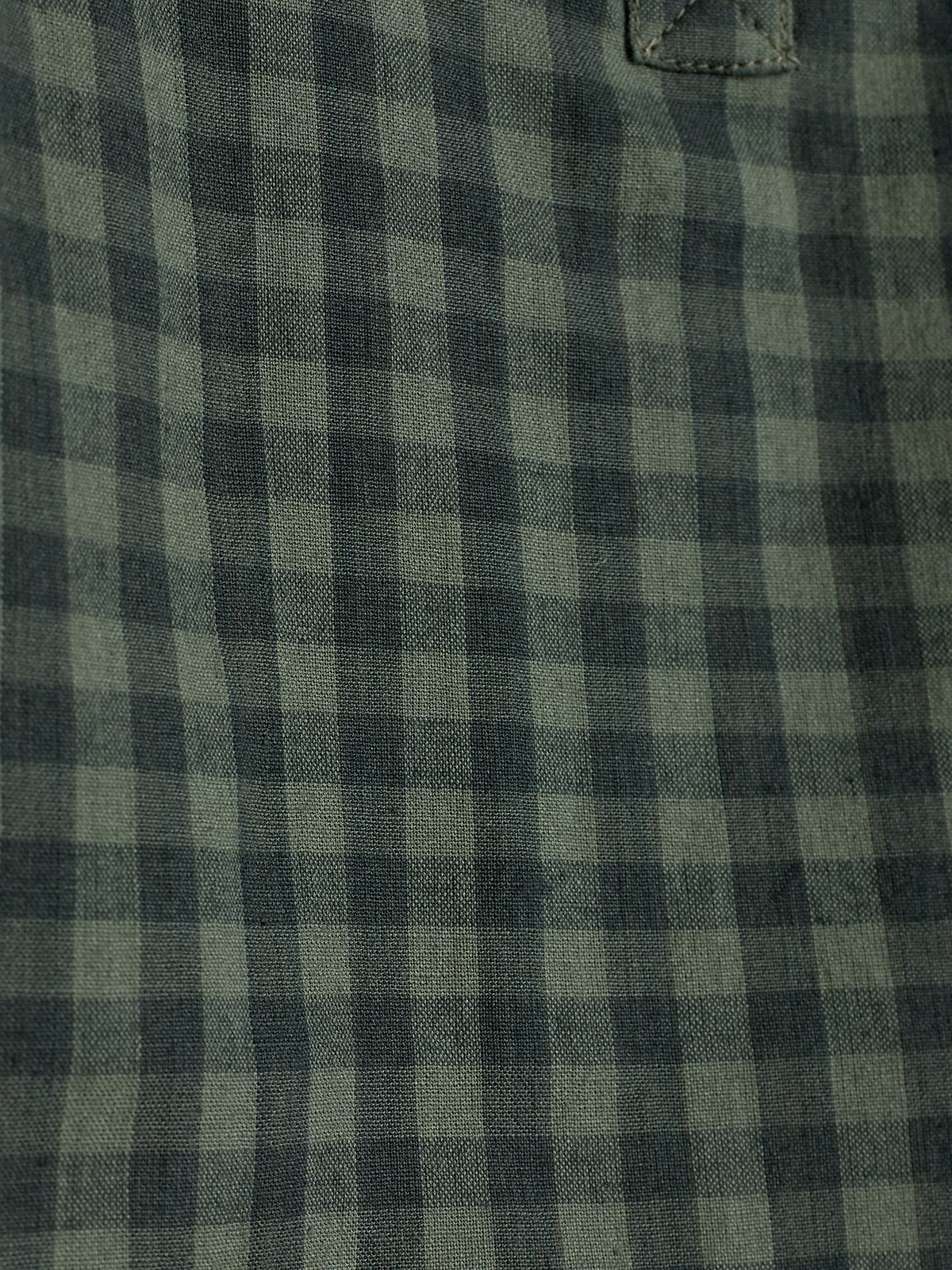 A fabric displays a black and green checkered pattern, suggesting a piece of clothing or upholstery, with visible stitching in a close-up view.