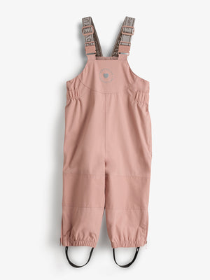 Pink overalls are hanging with adjustable straps and reinforced knee sections, featuring the text "FROM FIELD TO ADVENTURE" and a circular logo, against a plain white background.
