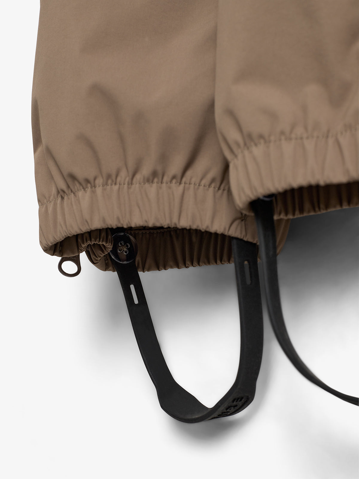 A beige jacket with elastic cuffs features adjustable black straps hanging below, set against a plain white background.