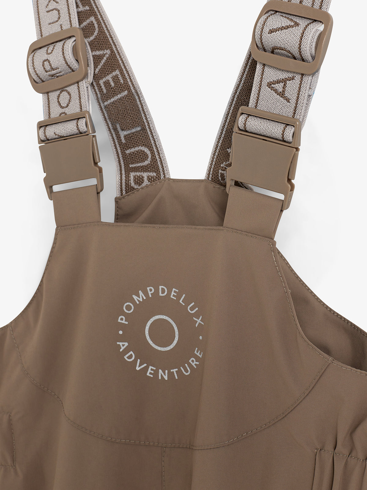 Brown suspenders with adjustable buckles are attached to a garment labeled "POMPDELUX ADVENTURE" in white text, against a plain, neutral background.