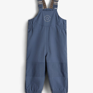 Blue children's overalls with adjustable shoulder straps and elasticized cuffs hang against a plain white background. "ROMPDELUX ADVENTURE" is printed on the chest.