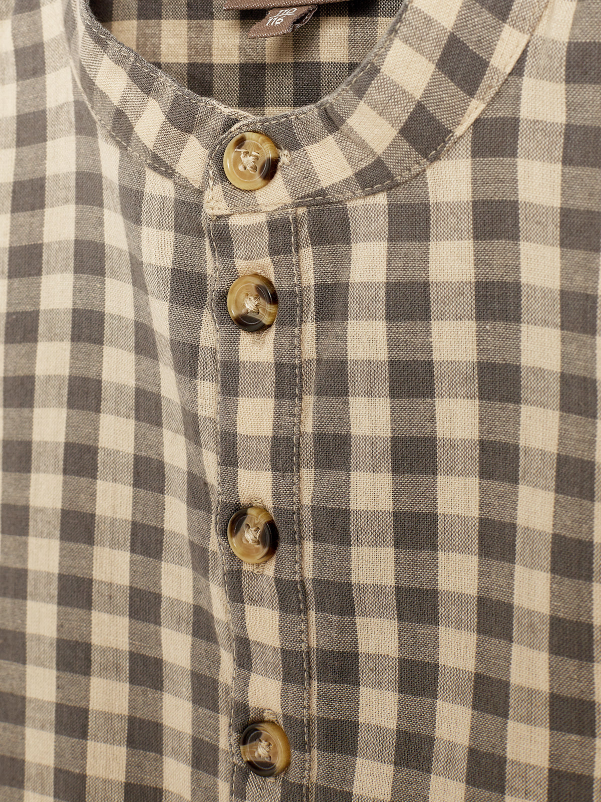 A close-up view of a checkered shirt with beige and dark gray squares. The shirt features a row of four brown buttons, and the collar is round and neatly stitched.